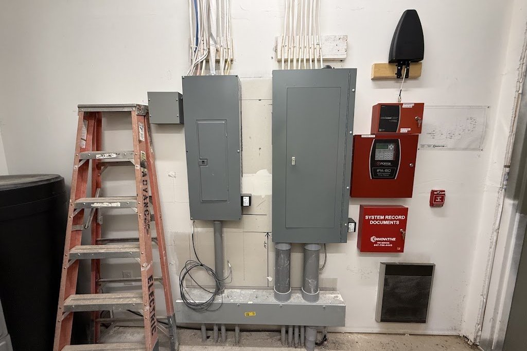 Commercial electrical panels with a fire alarm control panel and an Advanced Electric ladder in a building service room